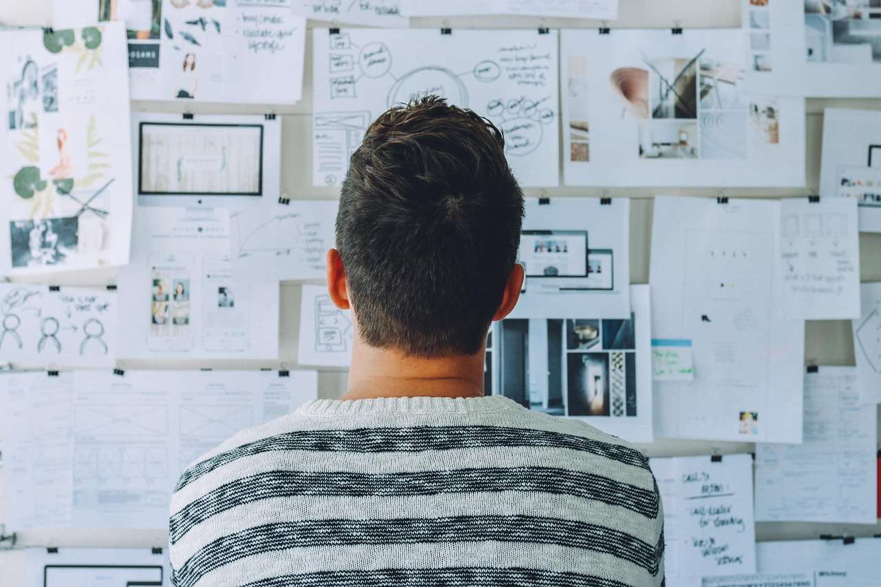 Student betrachtet eine Wand voller Notizen und Skizzen, Symbol für die Entwicklung und Entscheidung eines Forschungsansatzes.