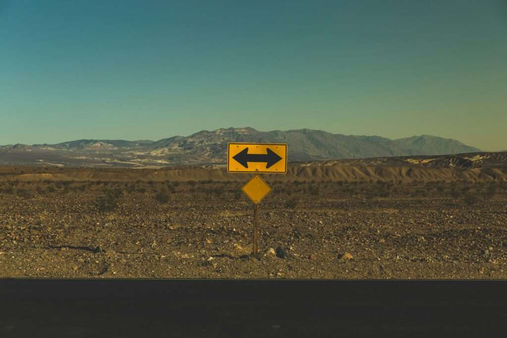 Wegweiser mit Pfeilen nach links und rechts in einer Wüstenlandschaft – Symbolbild für Entscheidungsfindung in der Forschung