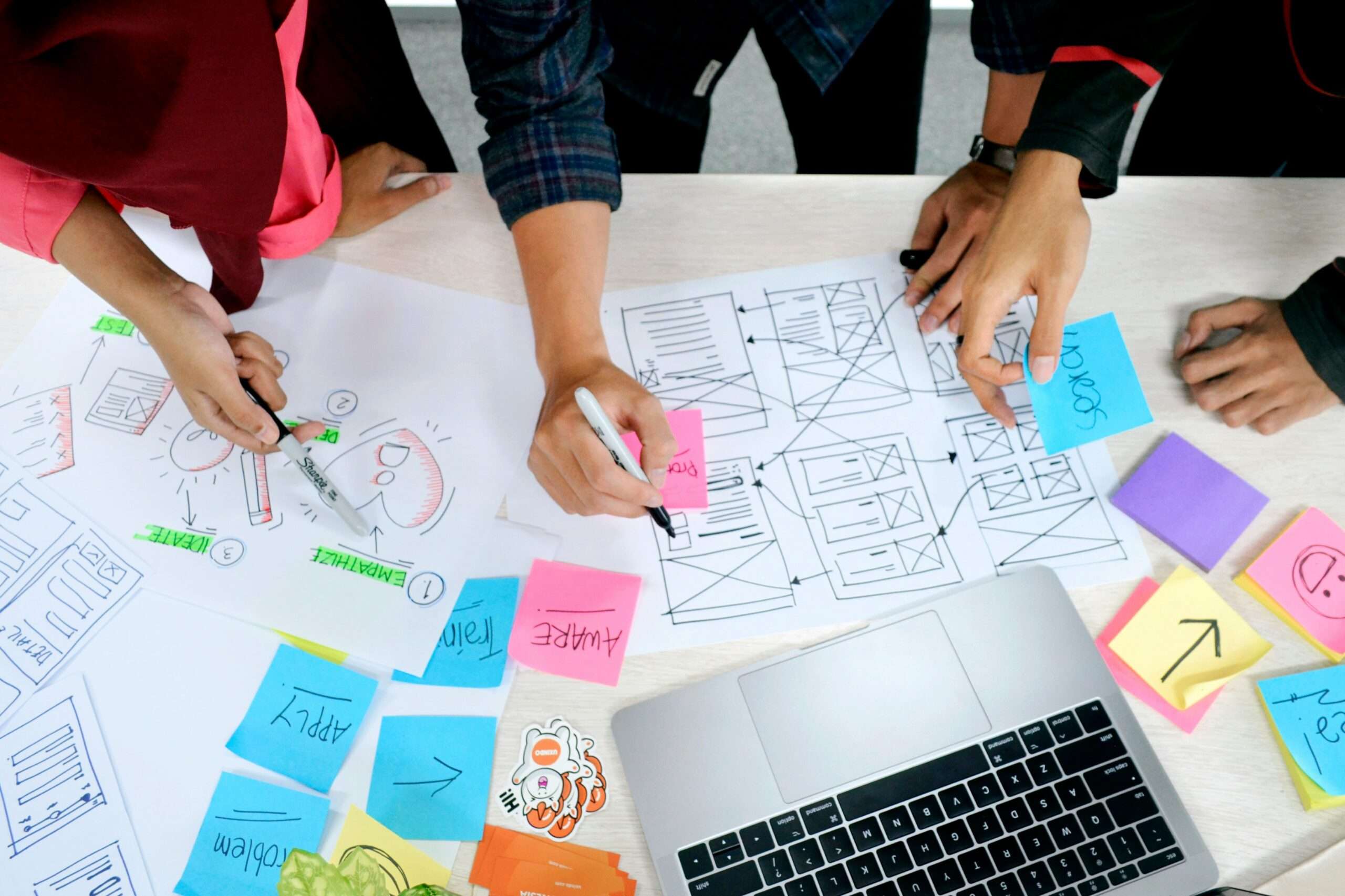 Studenten arbeiten an einem Schreibtisch mit Post Its und Dokumenten und brainstormen zur Themenfindung